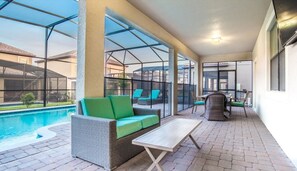 A covered outdoor area with a pool, wicker furniture, and a table. - Grhbtr1463 - Champions Gate Resort - 5 Bed 4 Baths House (Davenport)