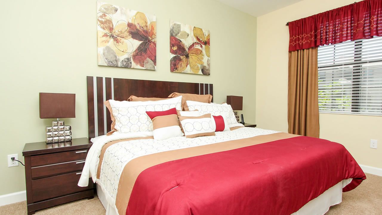 A bedroom with a large bed, two bedside tables, a nightstand, and a window with curtains.