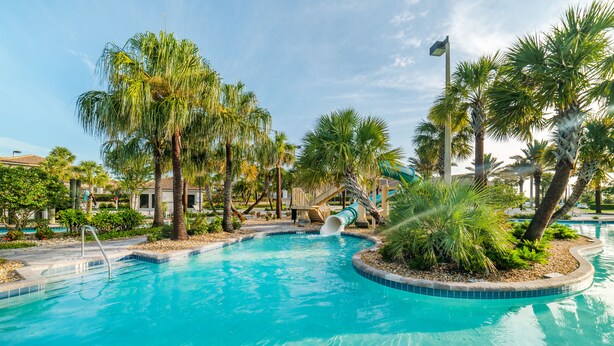 A swimming pool with a slide, surrounded by palm trees and a clear sky.