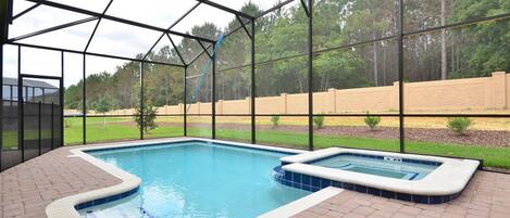 An indoor swimming pool with a hot tub, surrounded by a brick patio and a glass enclosure.