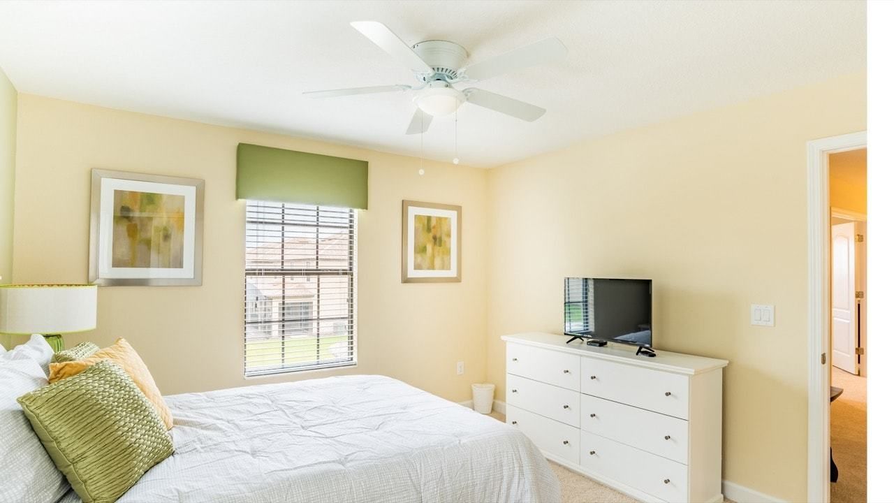 A bedroom with a bed, a dresser, a television, and a ceiling fan.