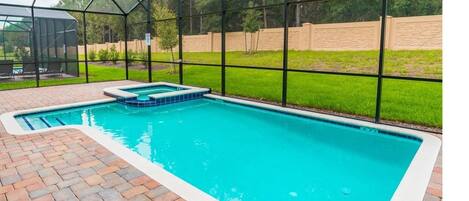 A rectangular pool with a blue interior, surrounded by a brick patio and a glass enclosure.