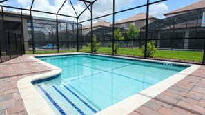 Une piscine rectangulaire dont le bord est recouvert de carreaux, entourée d’une terrasse en briques.
