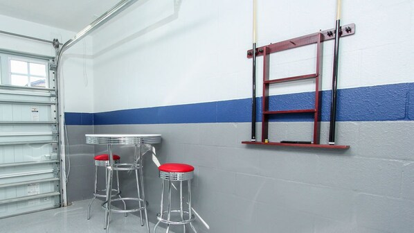 Une pièce avec un mur blanc et bleu, une échelle, deux tabourets avec des assises rouges et une table.
