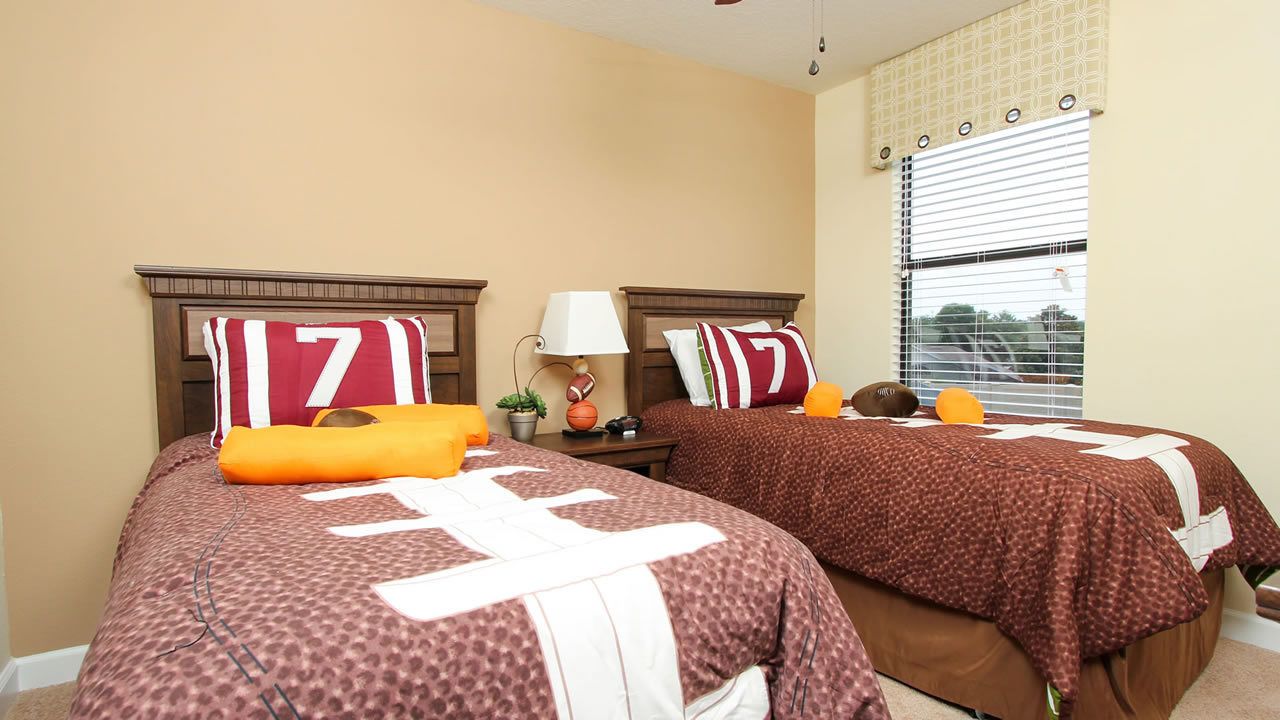 A bedroom with two beds, each with a headboard, a nightstand, a lamp, and a window with blinds.