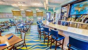 A restaurant with a bar area, multiple tables and chairs, and a patterned carpet.