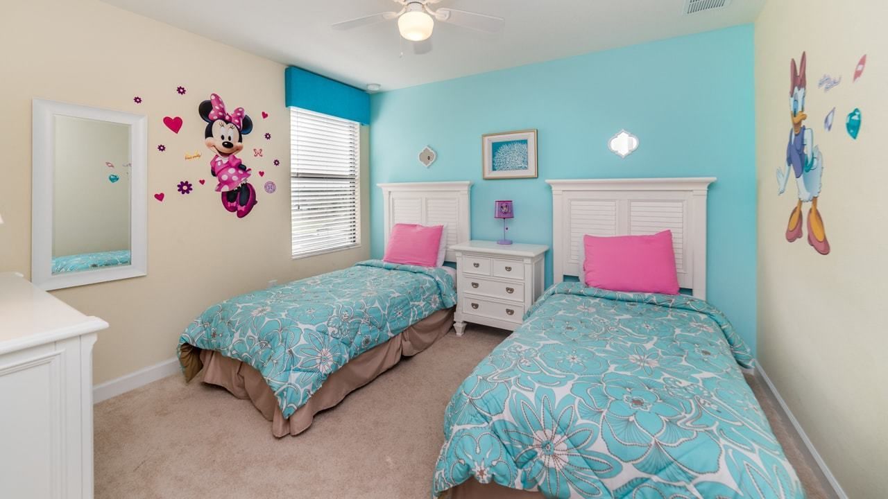 A bedroom with two beds, a dresser, a mirror, and a ceiling fan.