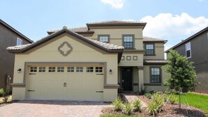A two-story house with a beige facade, a garage, and a well-maintained front yard with plants.
