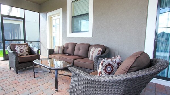 A covered patio area with wicker furniture, including a sofa set and a chair, and a glass-top table.
