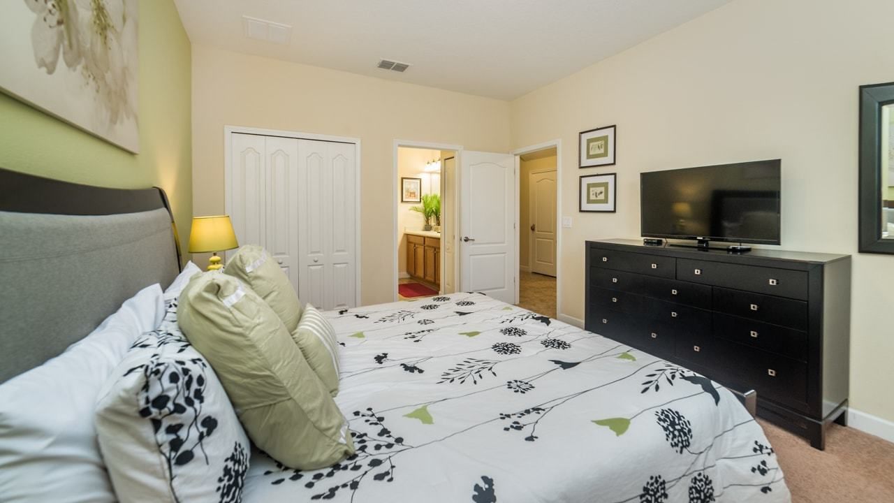 A bedroom with a bed, a dresser, a TV, and a door leading to a bathroom.
