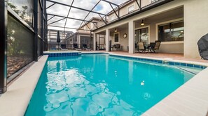A swimming pool with a glass enclosure, lounge chairs, and a covered patio area.