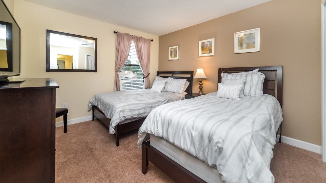 A hotel room with two beds, a dresser, a mirror, and a window with curtains.