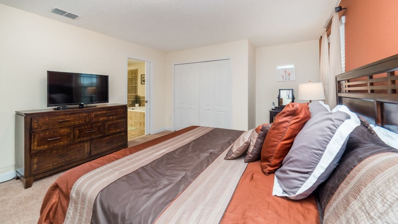 A bedroom with a bed, dresser, television, and a door leading to a bathroom.