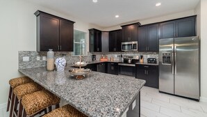 Cocina moderna con armarios oscuros, encimeras de granito, electrodomésticos de acero inoxidable y una zona de bar con taburetes.