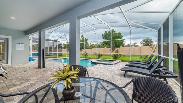 Un espacio exterior techado con piscina, sillas de descanso y una mesa con una planta.