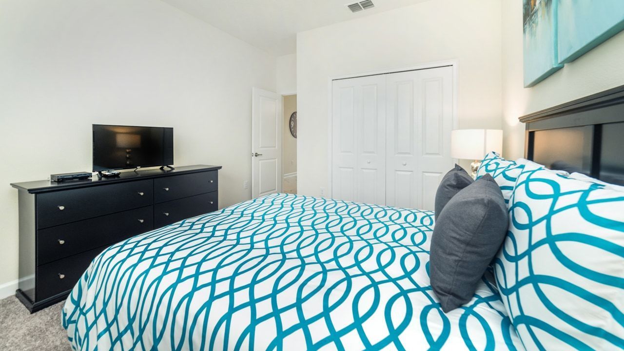 Ein Schlafzimmer mit Bett, Kommode, Fernseher und einer Tür.