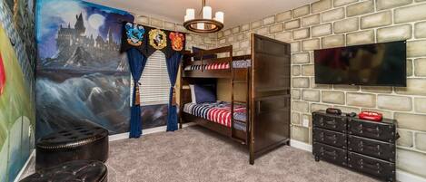 A room with a bunk bed, a flat-screen TV, a dresser, and a mural of a castle.