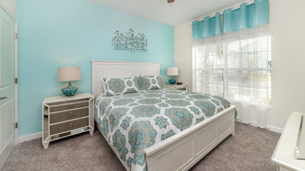 A bedroom with a bed, two bedside tables, a dresser, a window with curtains, and a wall art piece.