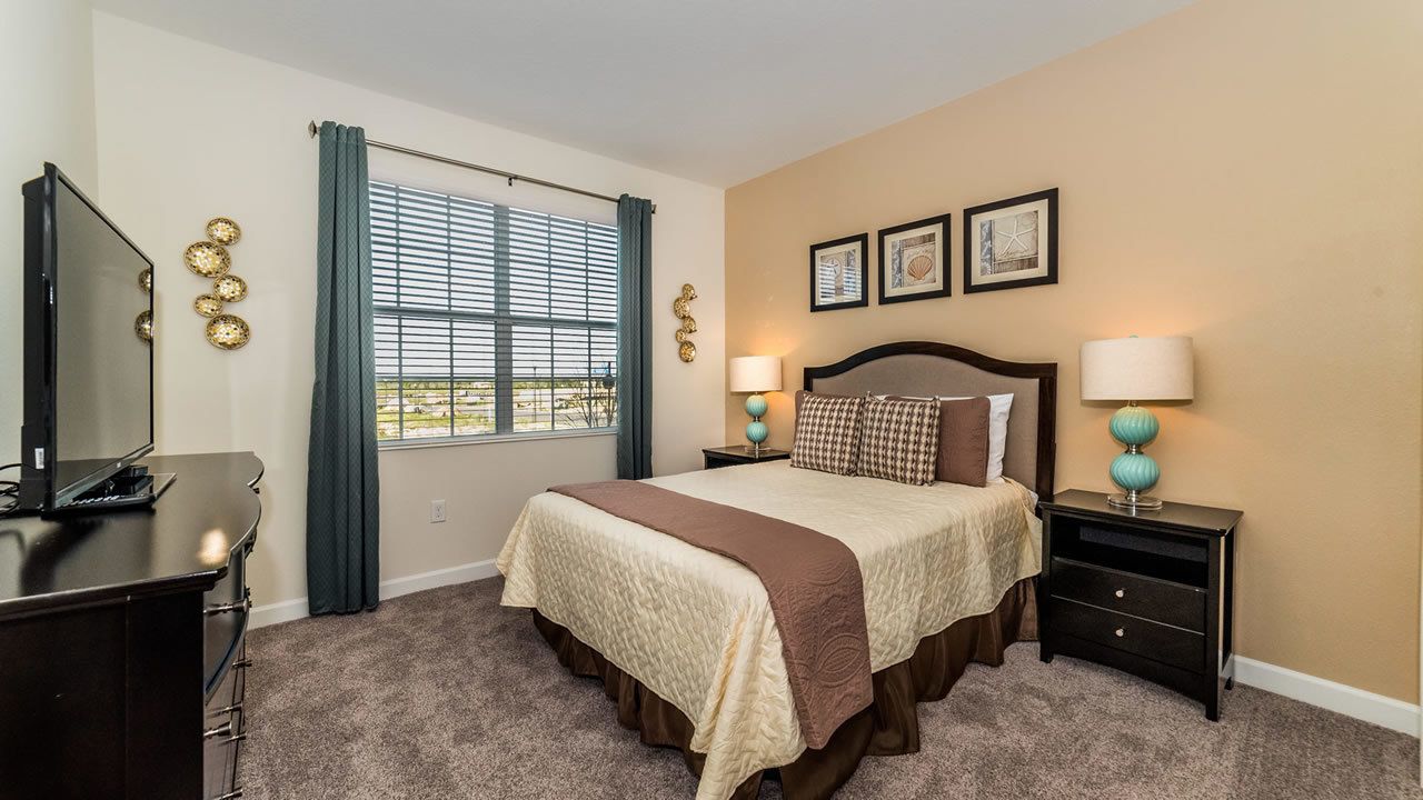 A bedroom with a bed, a TV, a desk, and a window with curtains.