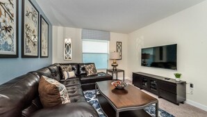 Un salon moderne avec un canapé d’angle en cuir, une table basse en bois, un téléviseur à écran plat et un meuble en bois foncé.