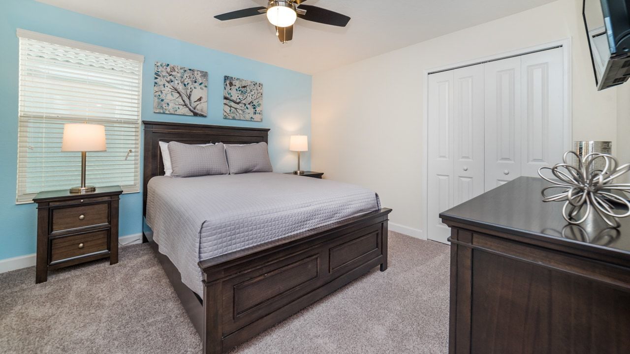 A bedroom with a bed, nightstands, a ceiling fan, a dresser, and a door.