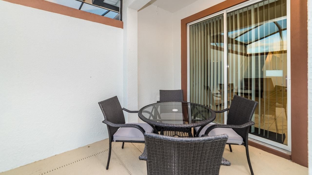 A balcony with a glass table and four wicker chairs.