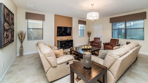 A living room with beige sofas, a coffee table, and a TV mounted on the wall. - Grhshm9028 - Champions Gate Resort - 6 Bed 6 Baths House (Davenport)