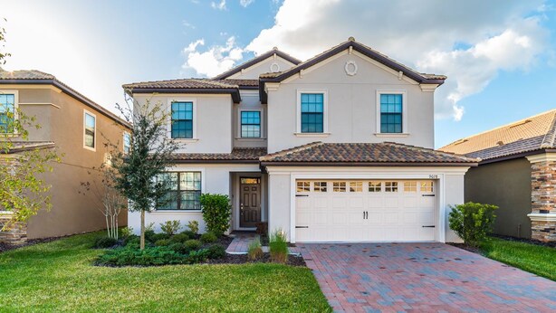 A two-story house with a garage, a front yard with a brick pathway, and a small garden area. - Grhshm9028 - Champions Gate Resort - 6 Bed 6 Baths House (Davenport)