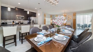 A modern dining area with a long wooden table set for six, surrounded by dark leather chairs.