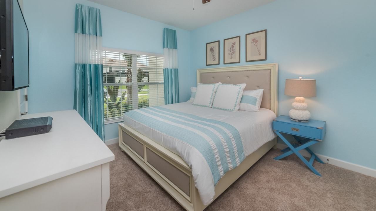 A bedroom with a bed, a desk, a nightstand, and a window with curtains.
