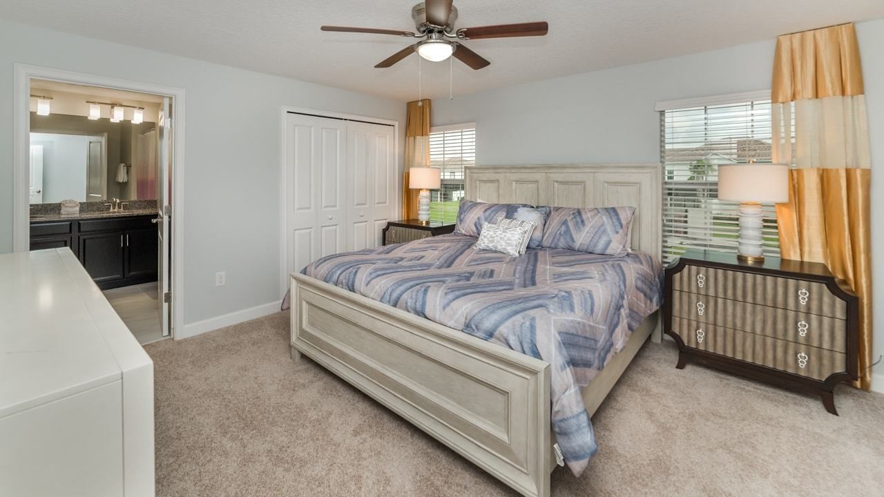 A bedroom with a bed, a ceiling fan, a nightstand, a dresser, and a window with blinds.