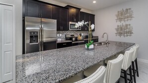 A modern kitchen with dark cabinets, stainless steel appliances, a granite countertop, and a decorative orchid.