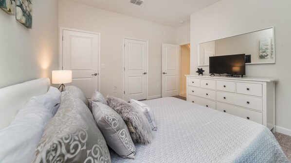 A bedroom with a bed, dresser, TV, and two doors.