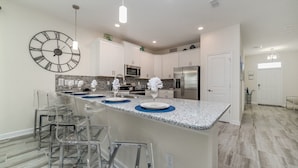 A modern kitchen with a central island, stainless steel appliances, and clear chairs. - Grhhzd9088 - Champions Gate Resort - 9 Bed 5 Baths House (Davenport)