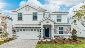 A two-story house with a white exterior, a stone accent wall, a garage, and a well-maintained lawn. - Grhhzd9088 - Champions Gate Resort - 9 Bed 5 Baths House (Davenport)