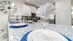A modern kitchen with a granite countertop, a clock on the wall, and a dining area with a glass vase and plates. - Grhhzd9088 - Champions Gate Resort - 9 Bed 5 Baths House (Davenport)
