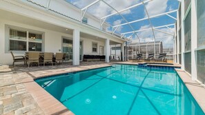 A swimming pool with a glass enclosure, lounge chairs, and a seating area with a sofa and table.