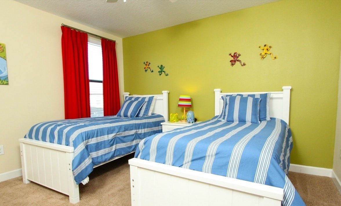 A bedroom with two beds, a window with red curtains, a lamp, and wall decorations.
