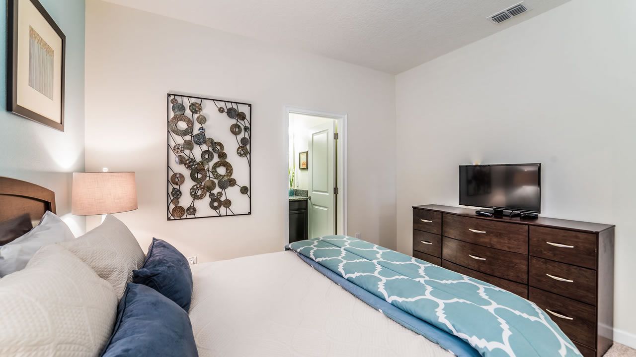 A bedroom with a bed, a dresser, a television, and a decorative wall piece.