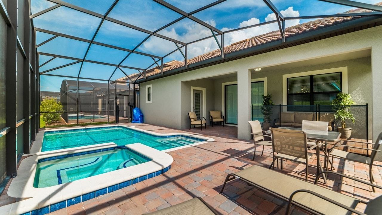A swimming pool with a glass enclosure, outdoor seating, and a patio area.