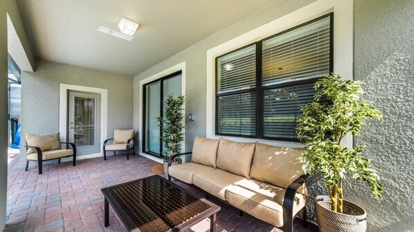 A sunlit patio with a beige sofa, two armchairs, a coffee table, and potted plants. - Grhwgd9165 - Champions Gate Resort - 4 Bed 3 Baths House (Davenport)