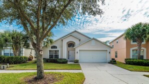 A two-story house with a garage, surrounded by well-maintained lawns and palm trees.