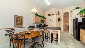 A modern kitchen with a dining area, wooden cabinets, a black refrigerator, and a hanging light fixture.