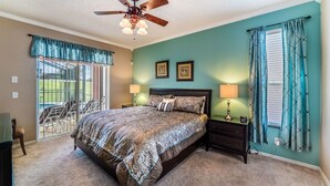 A bedroom with a bed, two bedside lamps, a ceiling fan, and a view of the outside through a sliding door.
