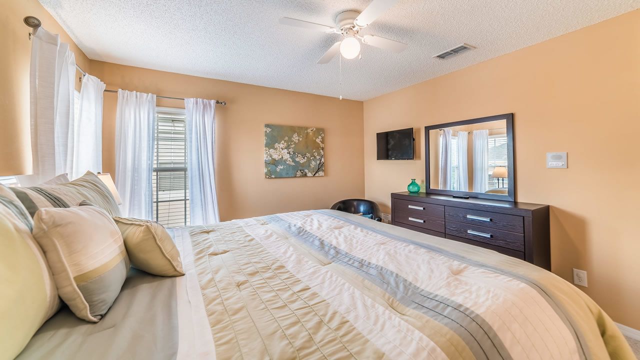 A bedroom with a bed, a dresser, a mirror, and a ceiling fan.