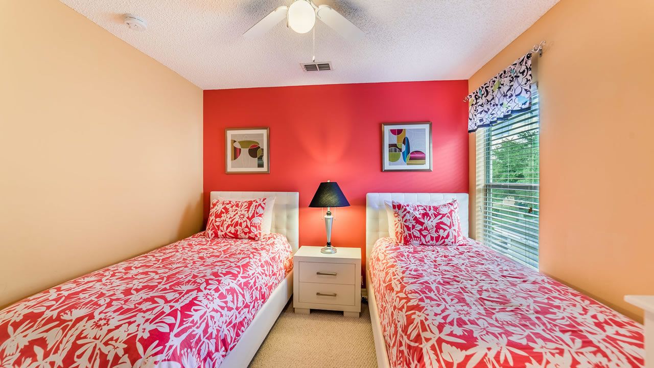 A bedroom with two beds, a nightstand with a lamp, and a ceiling fan.