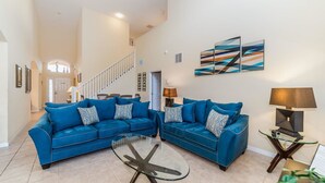 A spacious living room with two blue sofas, a glass coffee table, and a staircase leading to an upper level. - Grhokc8484 - Emerald Island Resort - 5 Bed 4 Baths House (Kissimmee)