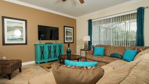 A living room with a sofa, a teal cabinet, a television, and artwork on the walls. - Grhbuc2967 - Paradise Palms Resort - 6 Bed 5 Baths House (Kissimmee)