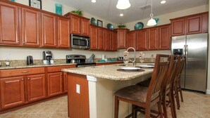 A kitchen with wooden cabinets, a granite countertop, stainless steel appliances, and a bar stool. - Grhbuc2967 - Paradise Palms Resort - 6 Bed 5 Baths House (Kissimmee)
