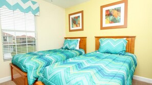 A bedroom with two beds, each with a blue and white chevron-patterned bedspread, wooden headboards, and two framed abstract paintings on the wall.